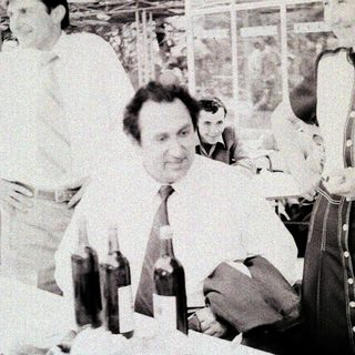 Group of men at an indoor event with wine bottles.