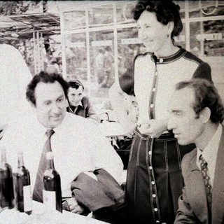 Group of men at an indoor event with wine bottles.