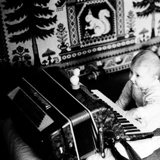 Baby playing with old accordion on couch.