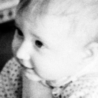 Baby playing with old accordion on couch.
