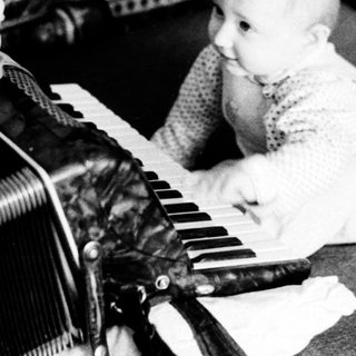 Baby playing with old accordion on couch.