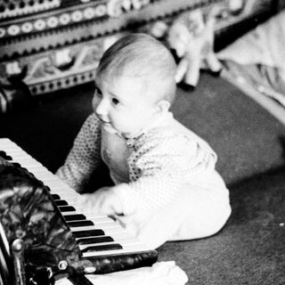 Baby playing with old accordion on couch.