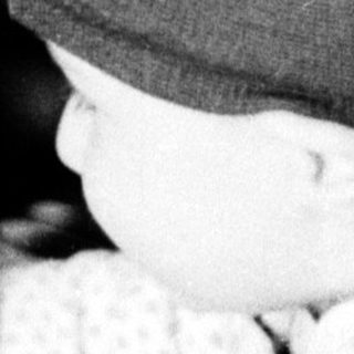 Baby wearing knit hat plays piano indoors.