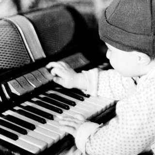 Baby wearing knit hat plays piano indoors.