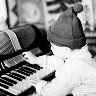 Baby wearing knit hat plays piano indoors.