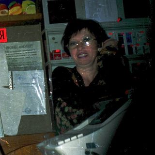 Two people posing behind a storefront with "For Sale" sign.