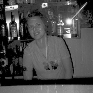 Barista smiling while holding two drinks behind a bar.