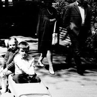 Two children riding toy cars outdoors.