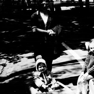Two children riding toy cars outdoors.
