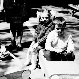 Two children playing with toy cars outdoors.