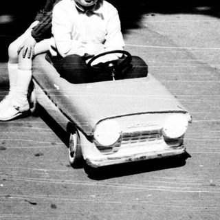 Child riding toy car on paved path.