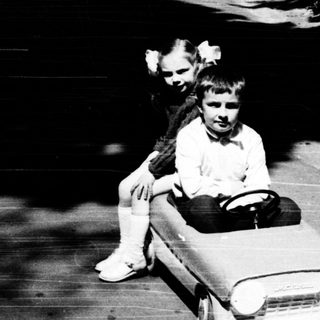 Child riding toy car on paved path.
