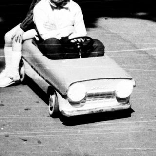Child riding toy car on paved path.