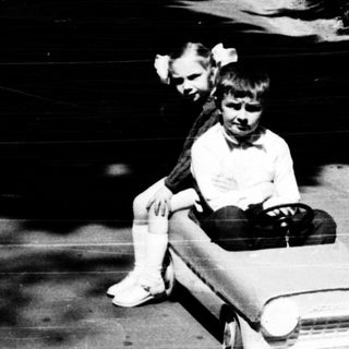 Child riding toy car on paved path.