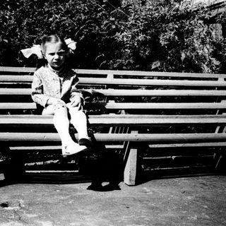 Young child sitting on wooden bench outdoors.