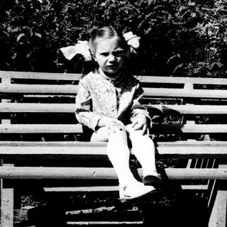 Young child sitting on wooden bench outdoors.