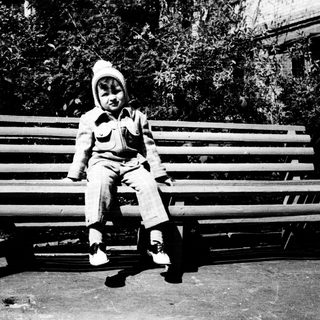 Child sitting on park bench outdoors.