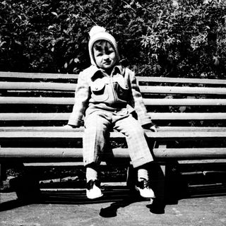 Child sitting on park bench outdoors.