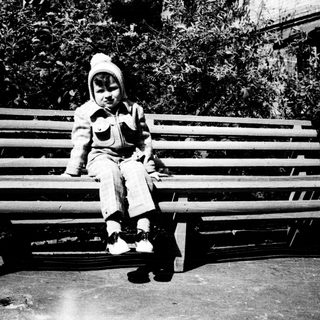 Child sitting on park bench outdoors.