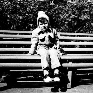 Child sitting on park bench outdoors.