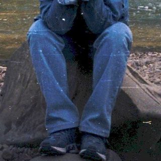 Person sitting on rocks by a flowing stream.
