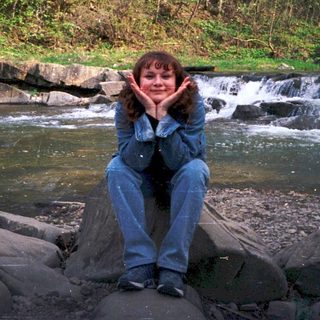 Person sitting on rocks by a flowing stream.