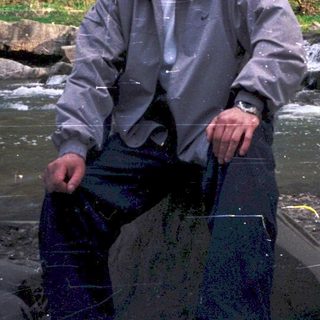 Man holding net by a flowing river with waterfall.