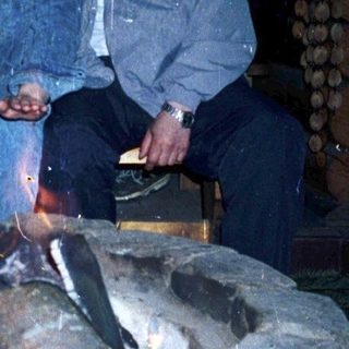 Two people sitting by a lit outdoor fire pit.