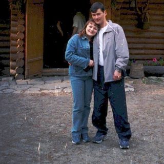 Two people posing outside rustic wooden cabin in forest.