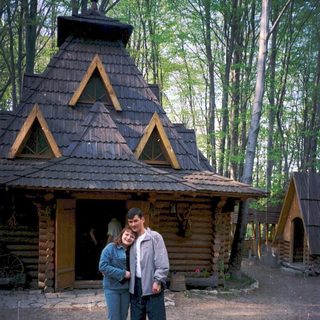 Two people posing outside rustic wooden cabin in forest.
