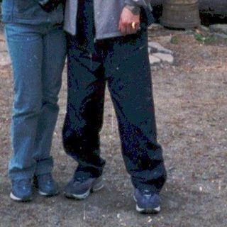 Two people posing outside rustic wooden cabin in forest.