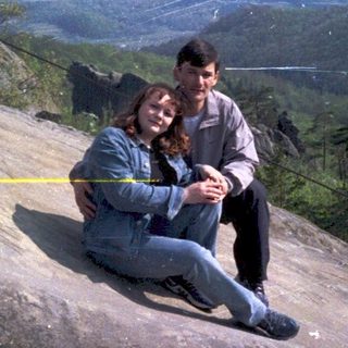 Couple sitting on rocky cliff overlooking scenic landscape.