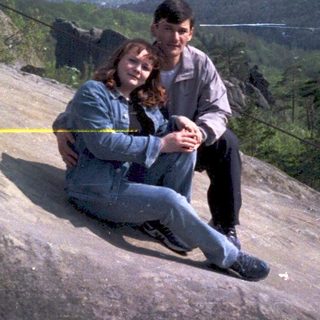 Couple sitting on rocky cliff overlooking scenic landscape.
