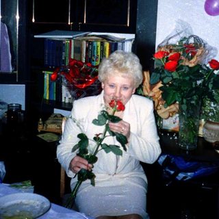 Elderly woman smelling rose at indoor celebration.