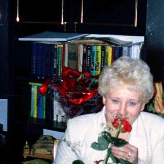 Elderly woman smelling rose at indoor celebration.