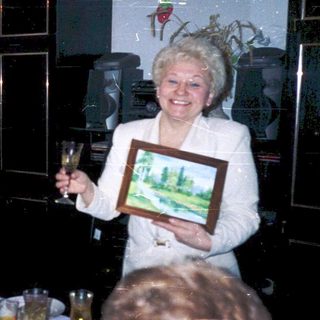Celebratory gathering with elderly couple holding framed artwork.