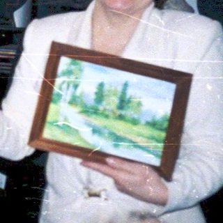 Celebratory gathering with elderly couple holding framed artwork.