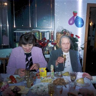 Three elderly women celebrating indoors with food and drinks.