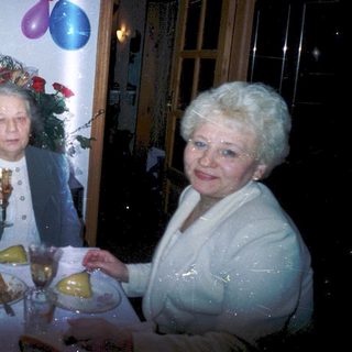 Three elderly women celebrating indoors with food and drinks.