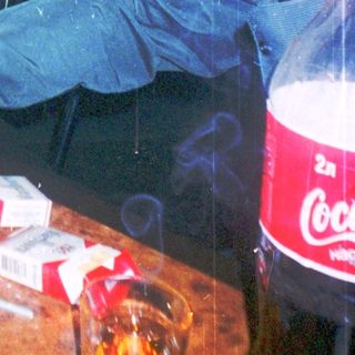 Person smokes near drink and snacks in dimly lit bar.
