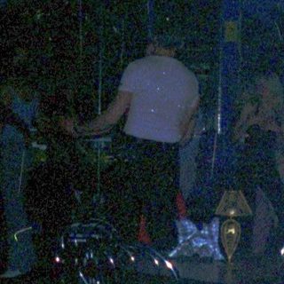 Person smokes near drink and snacks in dimly lit bar.