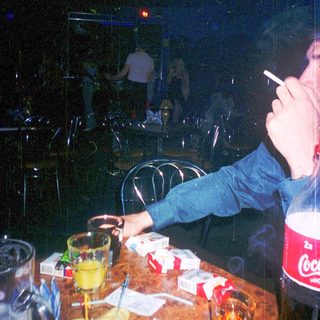 Person smokes near drink and snacks in dimly lit bar.