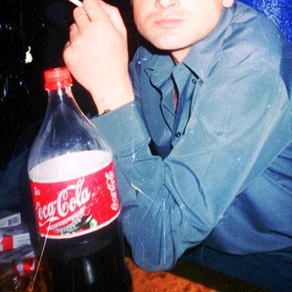 Man smoking near Coca-Cola bottle in dimly lit setting.