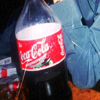 Man smoking near Coca-Cola bottle in dimly lit setting.