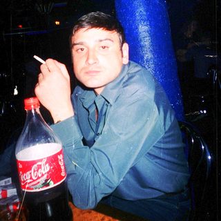 Man smoking near Coca-Cola bottle in dimly lit setting.