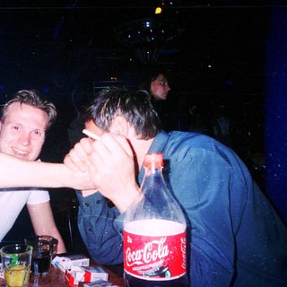Two men laughing together at a dimly lit table with drinks.