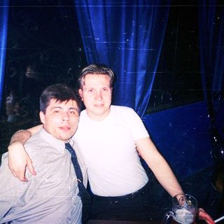 Two men posing indoors at nighttime event.