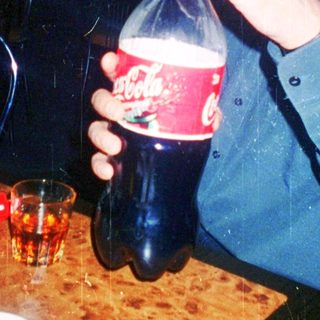 Man drinking soda indoors at a dimly lit table.