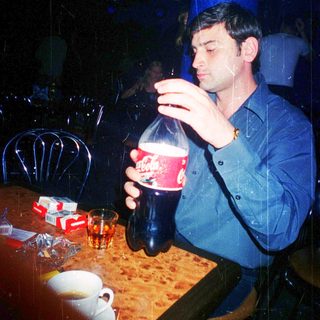 Man drinking soda indoors at a dimly lit table.