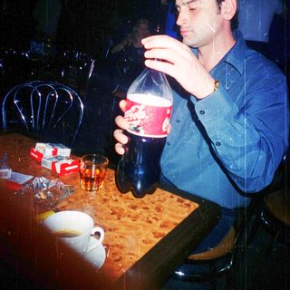 Man drinking soda indoors at a dimly lit table.
